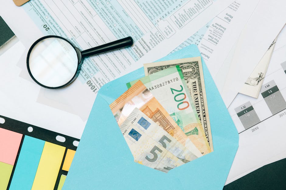 pieniądze w kopercie, lupa i dokumenty finansowe leżące na stole