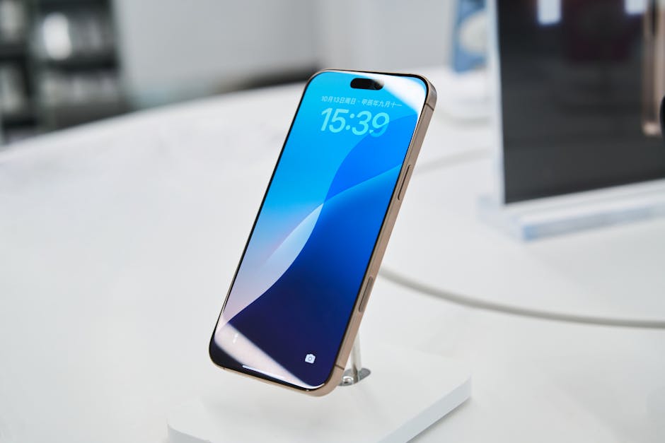 Smartfon marki Apple z włączonym wyświetlaczem stoi na białej podstawce.